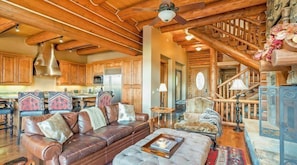 A rustic cabin interior with a wooden ceiling, a leather sofa, a dining area, and a staircase.