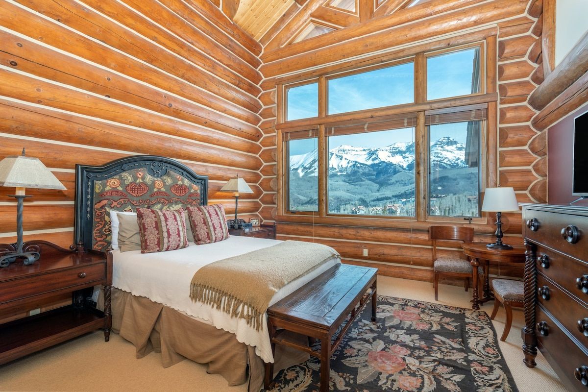 Une chambre située dans un chalet en rondins, avec un grand lit, deux tables de chevet, une commode et une vue sur des montagnes enneigées.