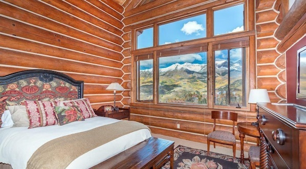 Une chambre aménagée dans un chalet en rondins, avec un lit, une chaise, une commode et une grande fenêtre donnant sur la montagne.
