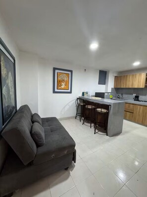 Una sala de estar moderna con un sofá gris, una zona de cocina con armarios de madera y un juego de taburetes de bar.