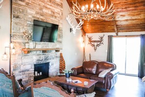 A rustic living room with a stone fireplace, leather sofa, and a mounted deer head. - Red Deer Lodge HiBanks Ranch 12 minutes from Magnolia Silos (Lorena)