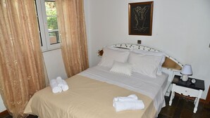 A neatly made bed with white linens and a beige bedspread, a bedside table with a lamp, and a framed artwork on the wall.