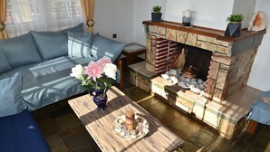 A living room with a sofa, a coffee table with decorative items, a fireplace with stone accents, and a small table with a vase of flowers.