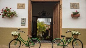 A building entrance with a wooden door, two bicycles with flower baskets, and a sign above the door.