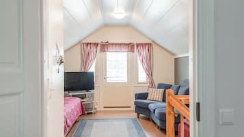 A cozy attic room with a television, sofa, and a window with curtains.