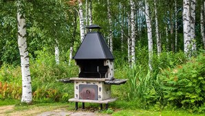 Un barbecue portatif installé dans un espace extérieur boisé, où l’on trouve des bouleaux.