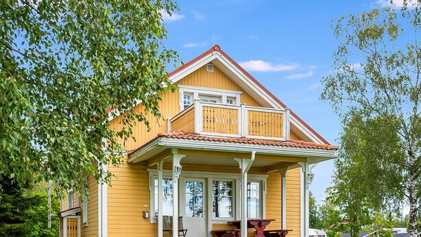 Une maison en bois jaune avec un balcon, une véranda dotée d’une table et de chaises, et une pelouse bien entretenue.