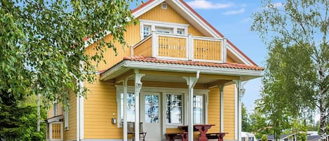 Ein gelbes Haus mit Balkon, Veranda und rotem Dach.