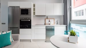 Une cuisine moderne avec des meubles blancs, un four encastré et un lave-vaisselle. On y trouve également un coin repas avec une table blanche et une plante en pot.