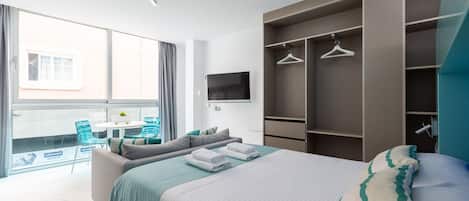 A modern hotel room with a large bed, a TV, a balcony with chairs, and a wardrobe with hangers.