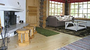 A rustic cabin interior with a stone wall, wooden furniture, and a large window providing natural light. - Rantapuro by Interhome (Kuusamo)