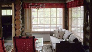 A cozy room with a wooden ceiling, a red chair, a white sofa, and a window with a red curtain. - Rantapuro by Interhome (Kuusamo)