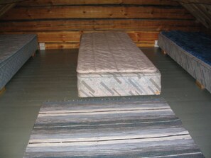 Een kamer met een groot centraal bed en twee kleinere aan weerszijden, houten wanden en een betonnen vloer.