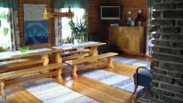 A rustic cabin interior with a wooden dining table, benches, a stone wall, and a television on the wall. - Rantala by Interhome (Kuusamo)