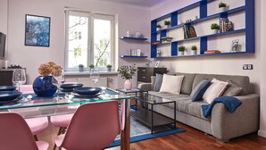 A modern living room with a glass dining table, pink chairs, a grey sofa, and blue shelving units. - Plac Zbawiciela Hipster Apartment (Warsaw)