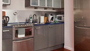 A compact kitchen with grey cabinets, a stainless steel stove, a microwave, and a refrigerator. - Plac Zbawiciela Hipster Apartment (Warsaw)