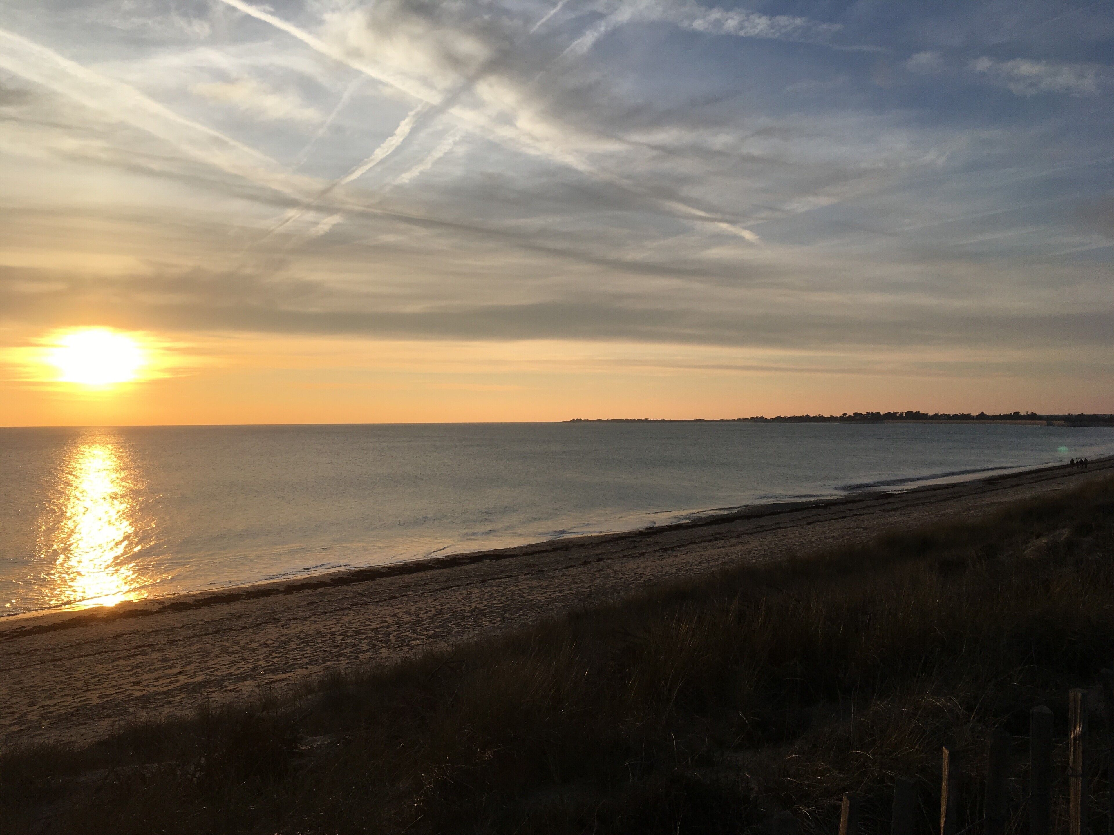 Une plage avec un ciel dégagé et le soleil se couchant sur l’eau.