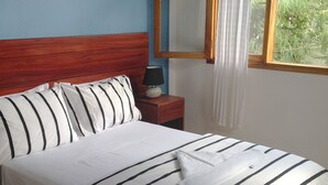 A bed with striped bedding, a wooden headboard, a nightstand with a lamp, and a window with curtains. - GALAPAGOS CASA MARINA (Puerto Ayora)