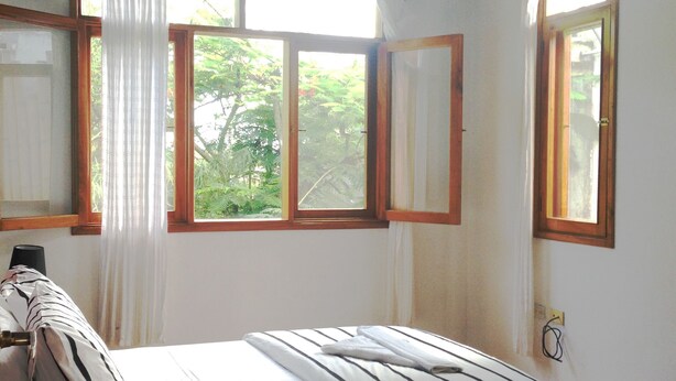 A bedroom with a bed, a wooden headboard, a bedside table, and a window with curtains. - GALAPAGOS CASA MARINA (Puerto Ayora)
