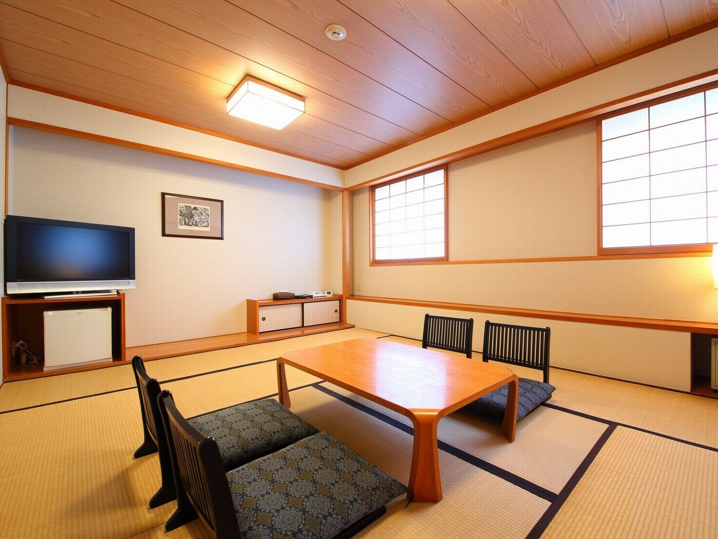 A traditional Japanese room with tatami flooring, a low table, chairs, a television, and a window with shoji screens.