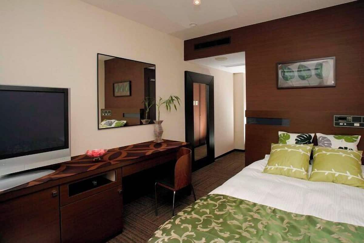 Een hotelkamer met een bed, bureau, televisie, spiegel en deur.
