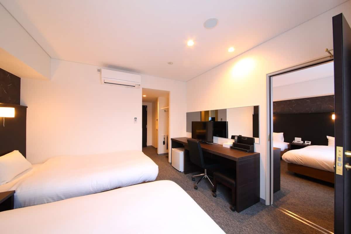 Een hotelkamer met twee bedden, een bureau met een computer, een televisie en een airconditioning.
