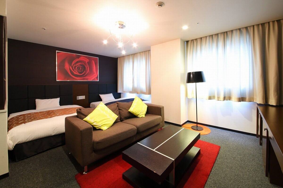 Een hotelkamer met een bed, een bank met kussens, een salontafel, een rood tapijt, een vloerlamp en een groot rood kunstwerk aan de muur.