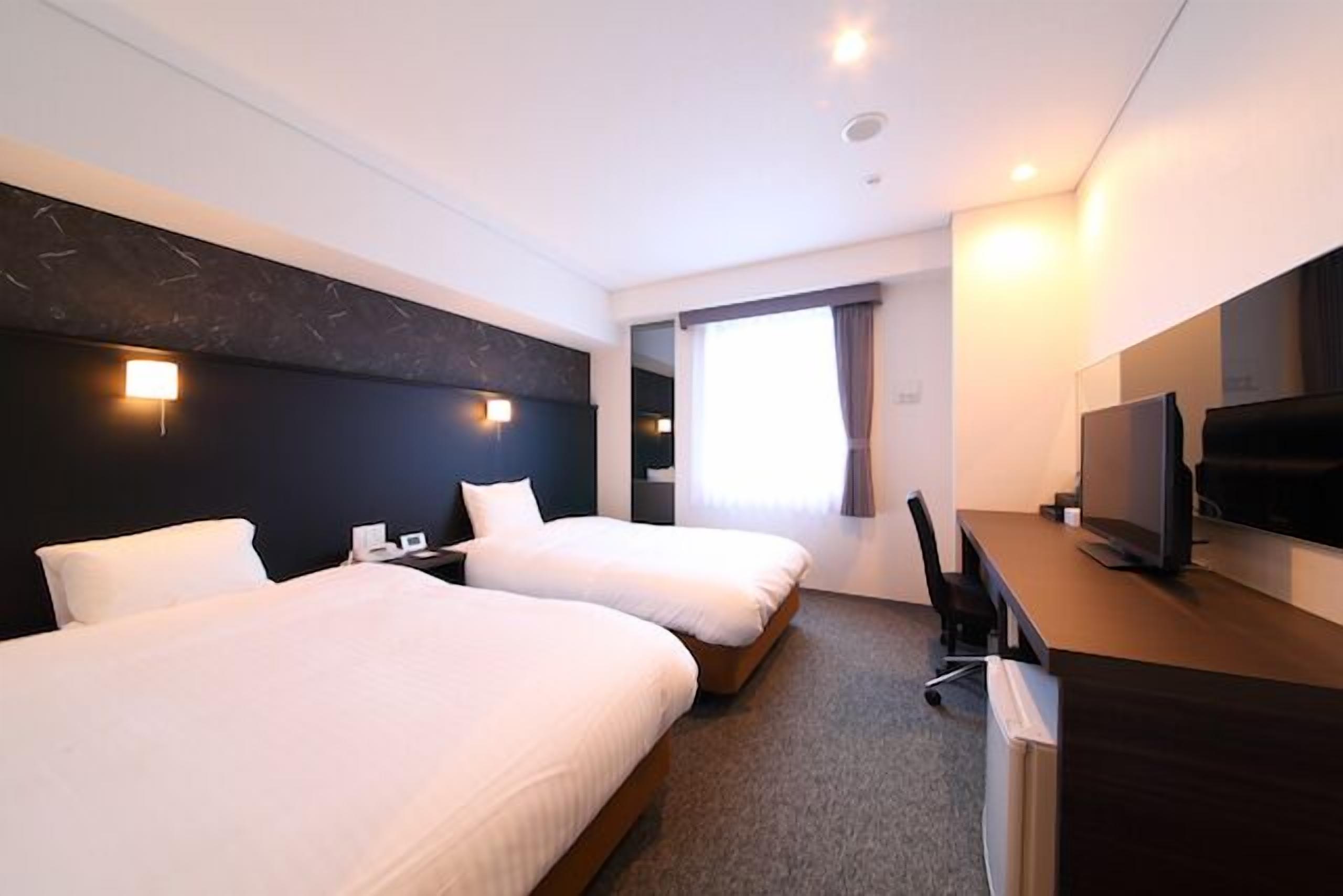 A hotel room with two beds, a desk, a television, and a window with curtains.