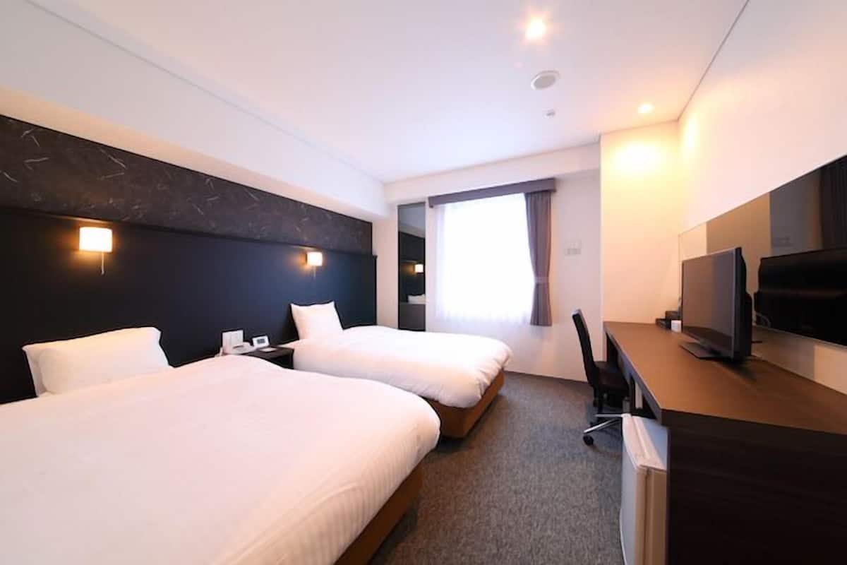 Een hotelkamer met twee bedden, een bureau, een televisie en een raam met gordijnen.