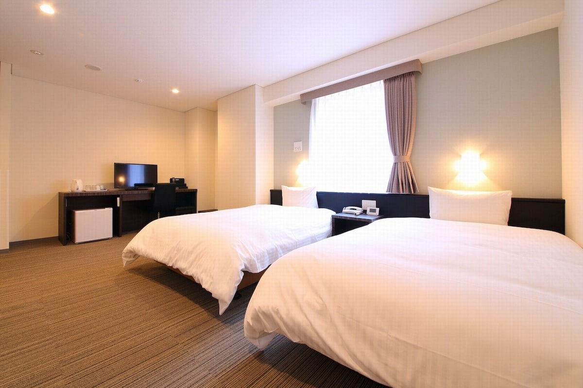 Een hotelkamer met twee bedden, een televisie, een bureau met een computer en een raam met gordijnen.