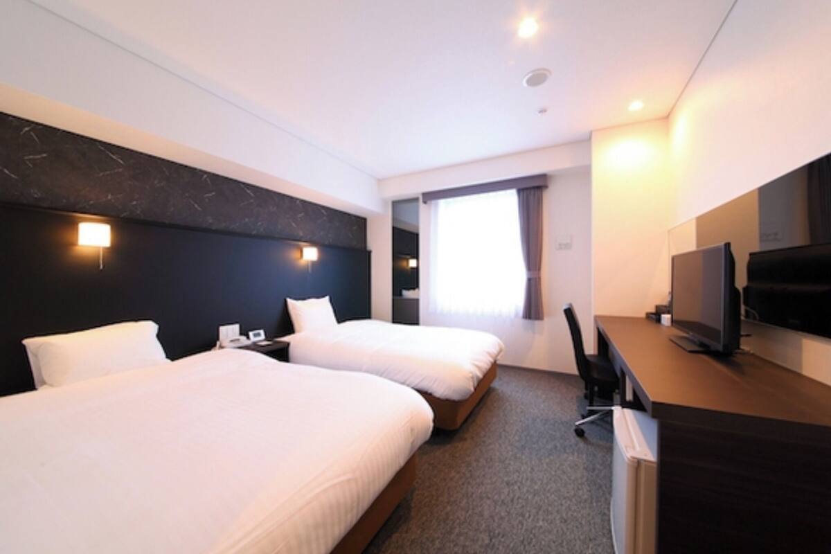 Een hotelkamer met twee bedden, een bureau, een televisie en een raam met gordijnen.