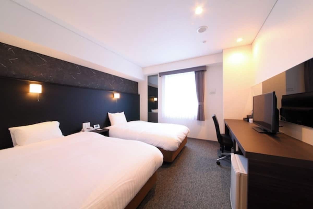 Habitación de hotel con dos camas, un escritorio, un televisor y una ventana con cortinas.
