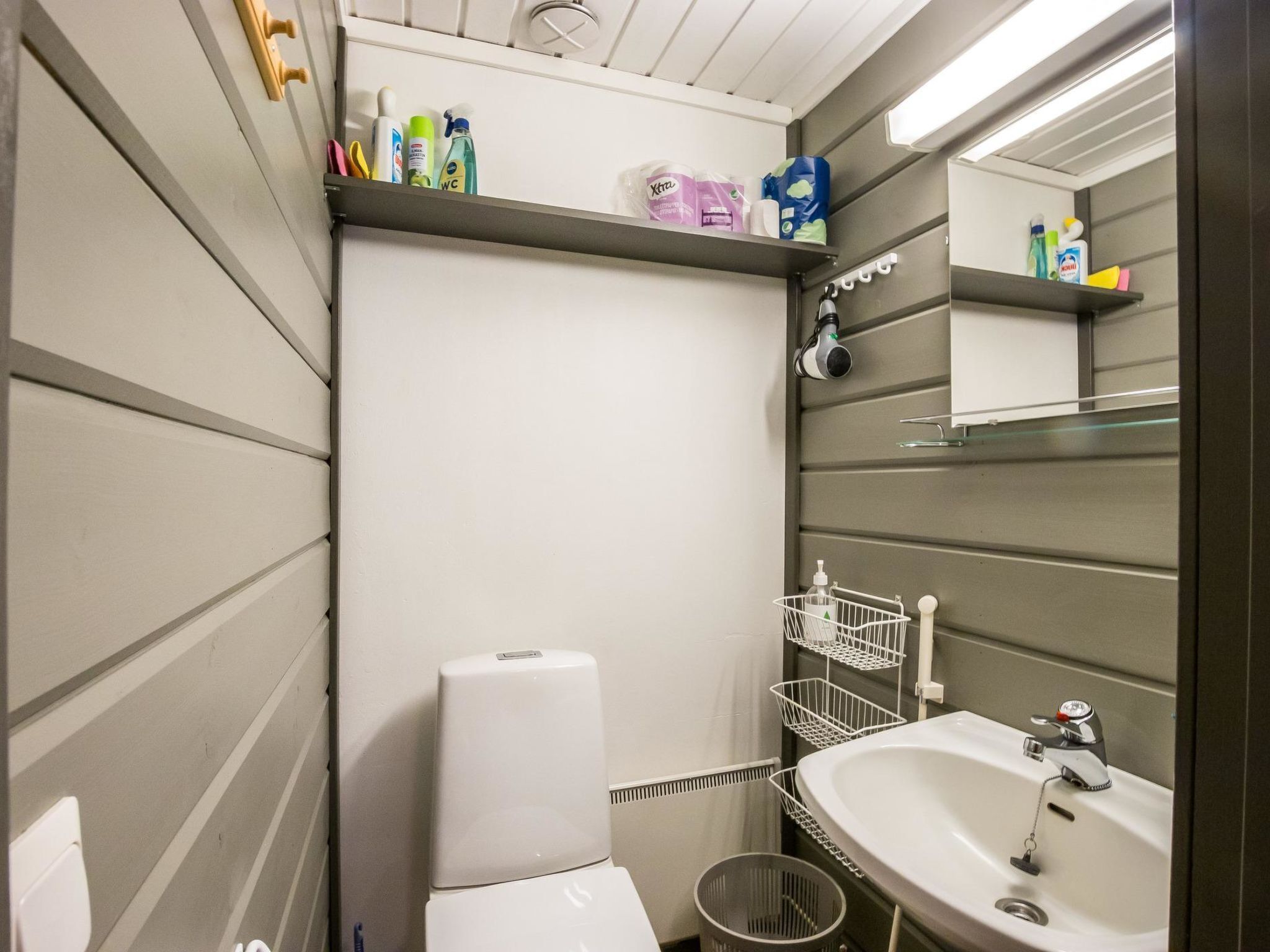 A bathroom with a toilet, sink, and shelves with toiletries.