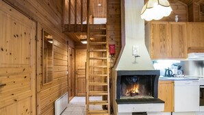 L’intérieur d’une cabane en bois comprend une cheminée, une échelle menant à une mezzanine et un coin cuisine.