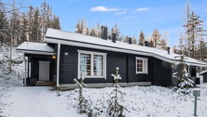 Une maison en bois noire, avec un toit recouvert de neige et un petit porche.