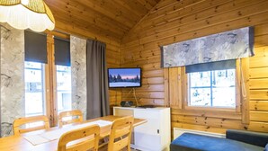 L’intérieur chaleureux d’un chalet avec une table à manger en bois, des chaises, un canapé, un téléviseur et une radio.