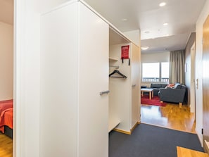 A hotel room with a wardrobe, a bed, a seating area with a sofa and a table, and a window with curtains.