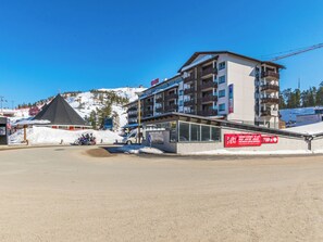 A multi-story hotel with balconies, a ski slope in the background, and a sign indicating a restaurant.