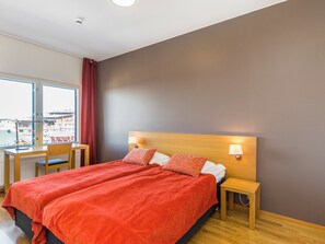 Une chambre d’hôtel avec un grand lit, un bureau, une chaise et une fenêtre donnant sur des immeubles.