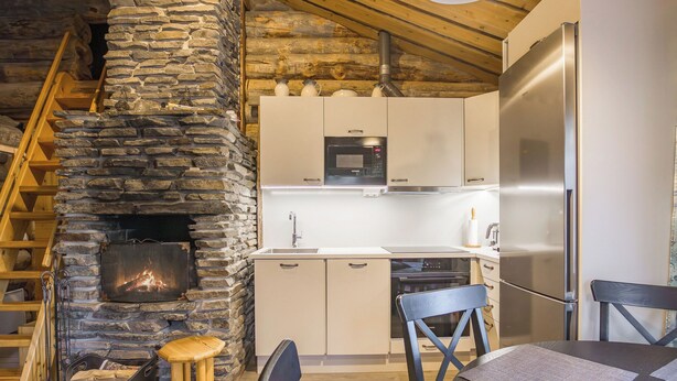 Eine rustikale Küche mit Kamin aus Stein, Holzbalken und modernen Geräten.