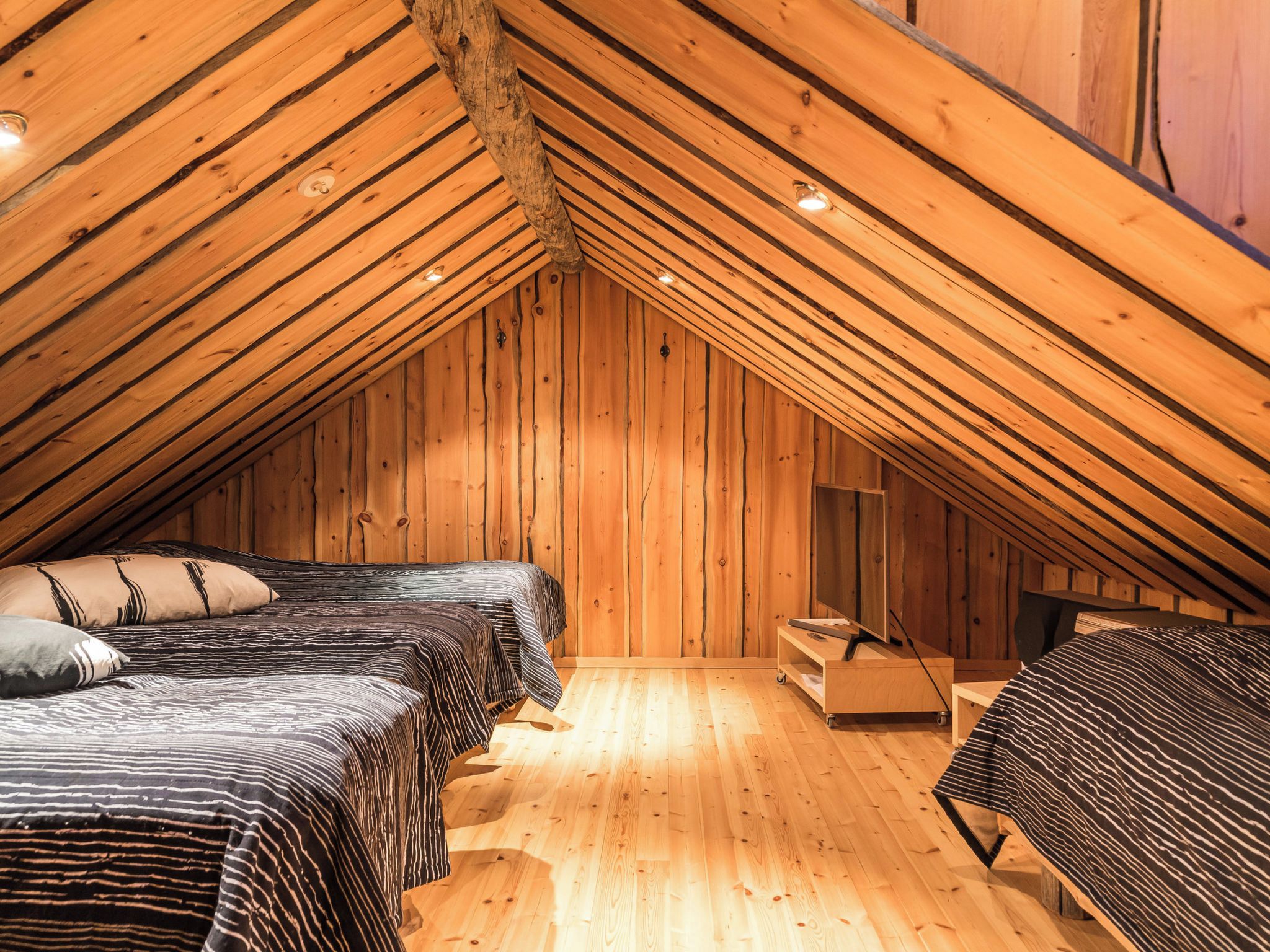 A cozy attic bedroom with wooden walls and sloped ceilings, featuring two beds with striped bedding and a small desk.