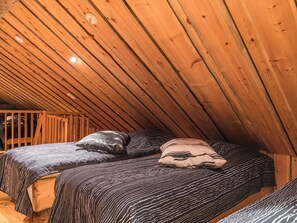 A loft bedroom with a sloped ceiling and wooden beams, featuring two beds with striped bedding and multiple pillows.