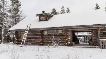 A log cabin with a snow-covered roof, a ladder, and a small porch area.