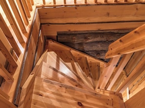 A wooden staircase leading to an attic space with exposed beams and a sloped ceiling.