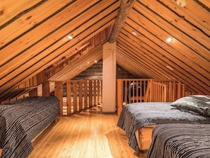 A cozy attic bedroom with wooden beams, two beds, and a sloped ceiling.