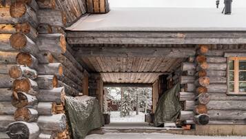 A log cabin with a snow-covered entrance, wooden logs on the walls, and a window on the right side.