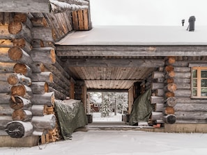 A log cabin with a snow-covered entrance, wooden logs on the walls, and a window on the right side.