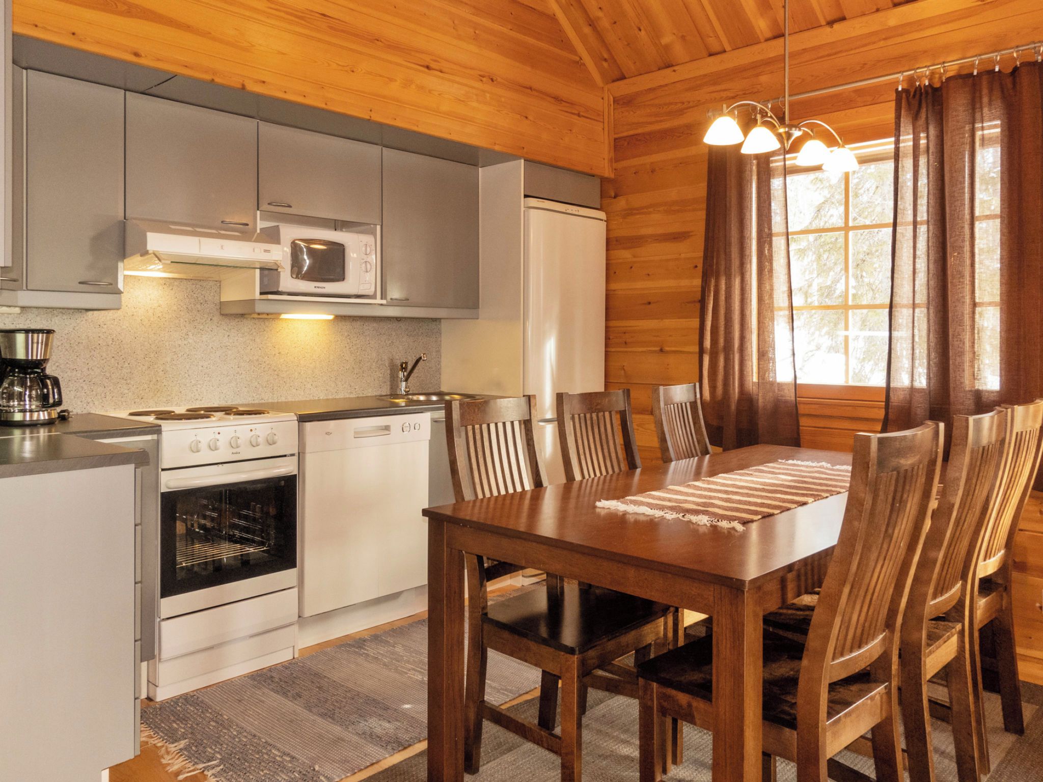 A wooden cabin interior with a kitchen, dining table, and chairs.
