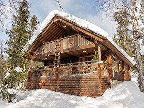Una baita di legno con un balcone, circondata da neve e alberi.