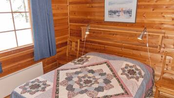 A cozy room with a wooden interior, a bed with a floral quilt, a window with a view, and a painting on the wall.